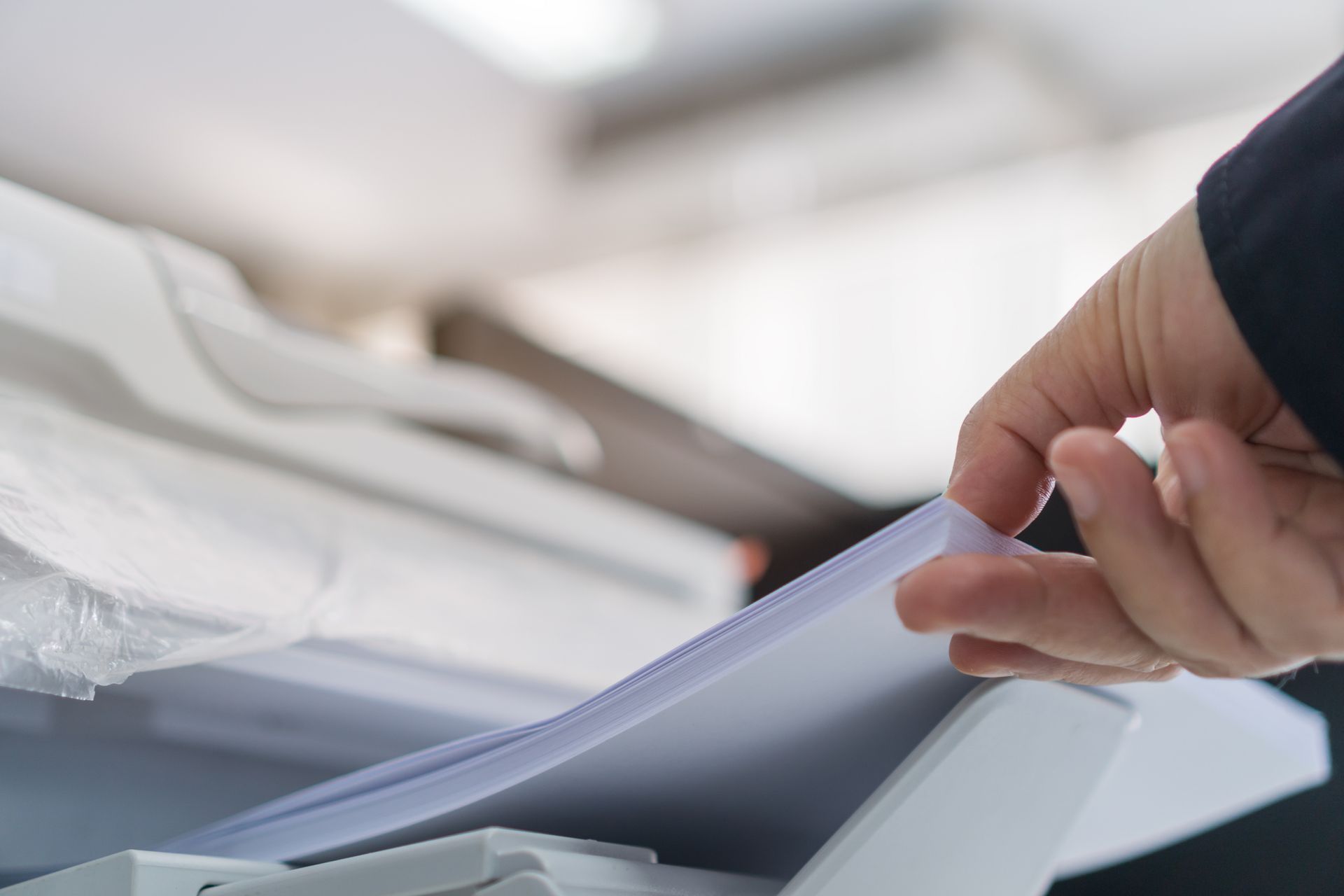 Hand taking a stack of papers from a printer's output tray.