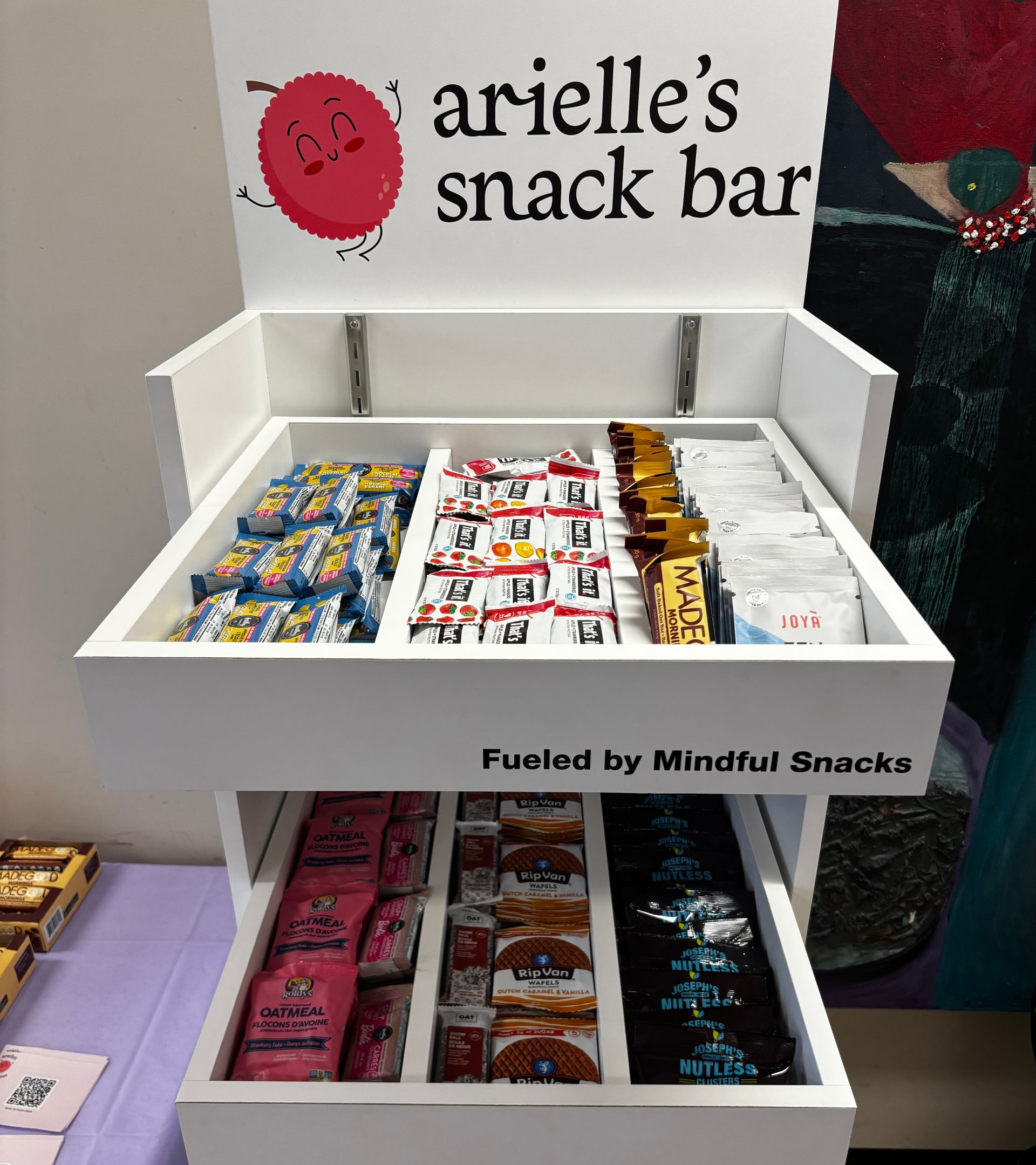 Snack display stand with assorted colorful candy bars labeled “arielle’s snack bar”