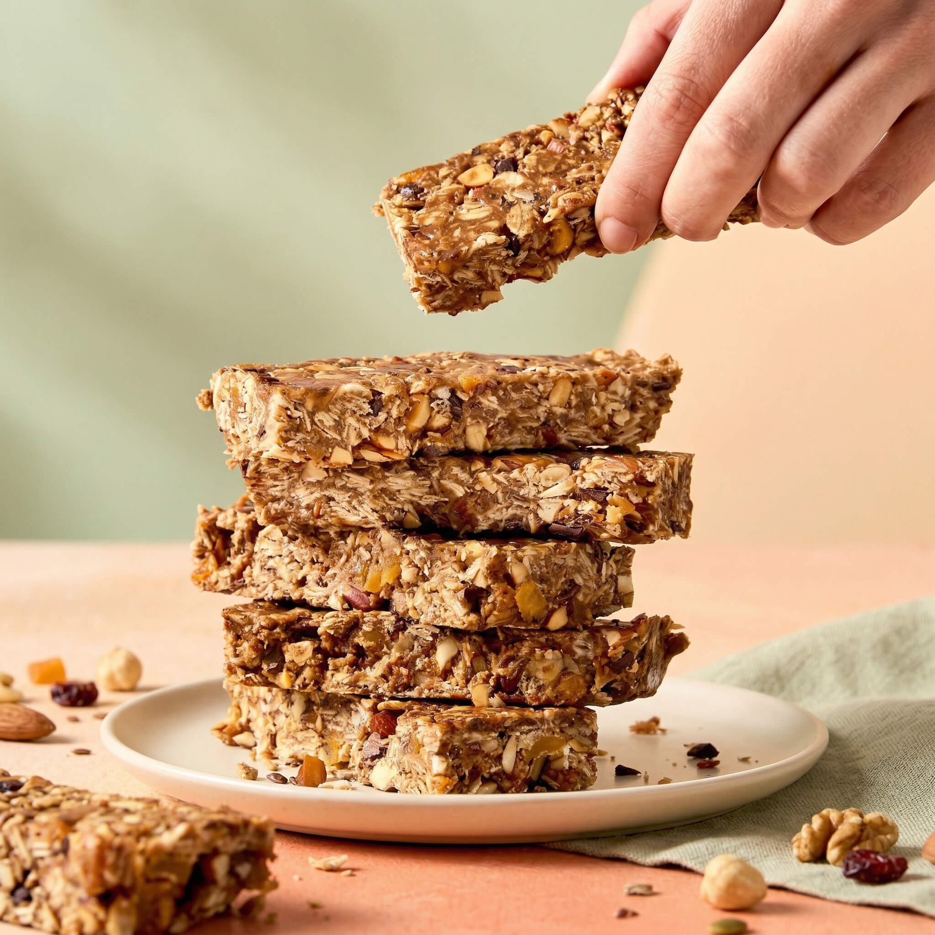 Hand stacking granola bars on a plate, with more bars and crumbs on a pastel tabletop