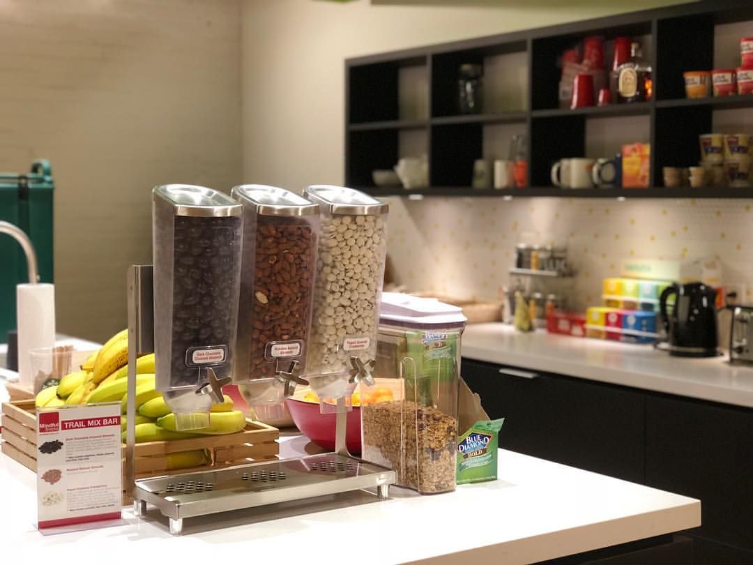 Modern kitchen countertop with cereal dispensers, fruit, mugs, and open shelving with cups and jars