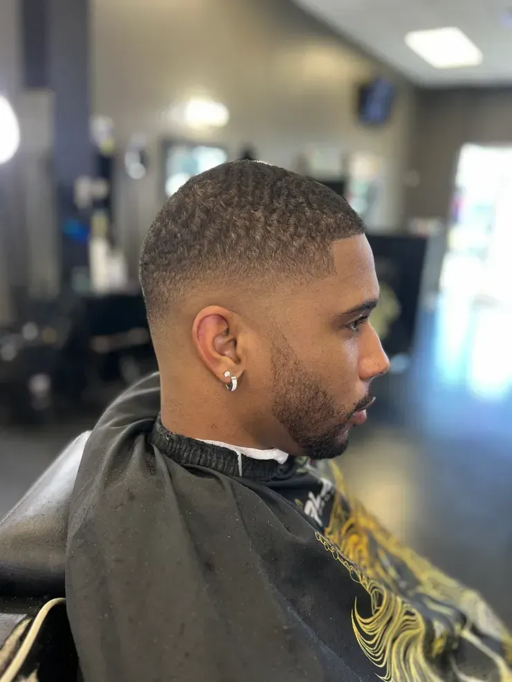 Side-profile haircut in a barbershop, with a faded cut and gold earring.