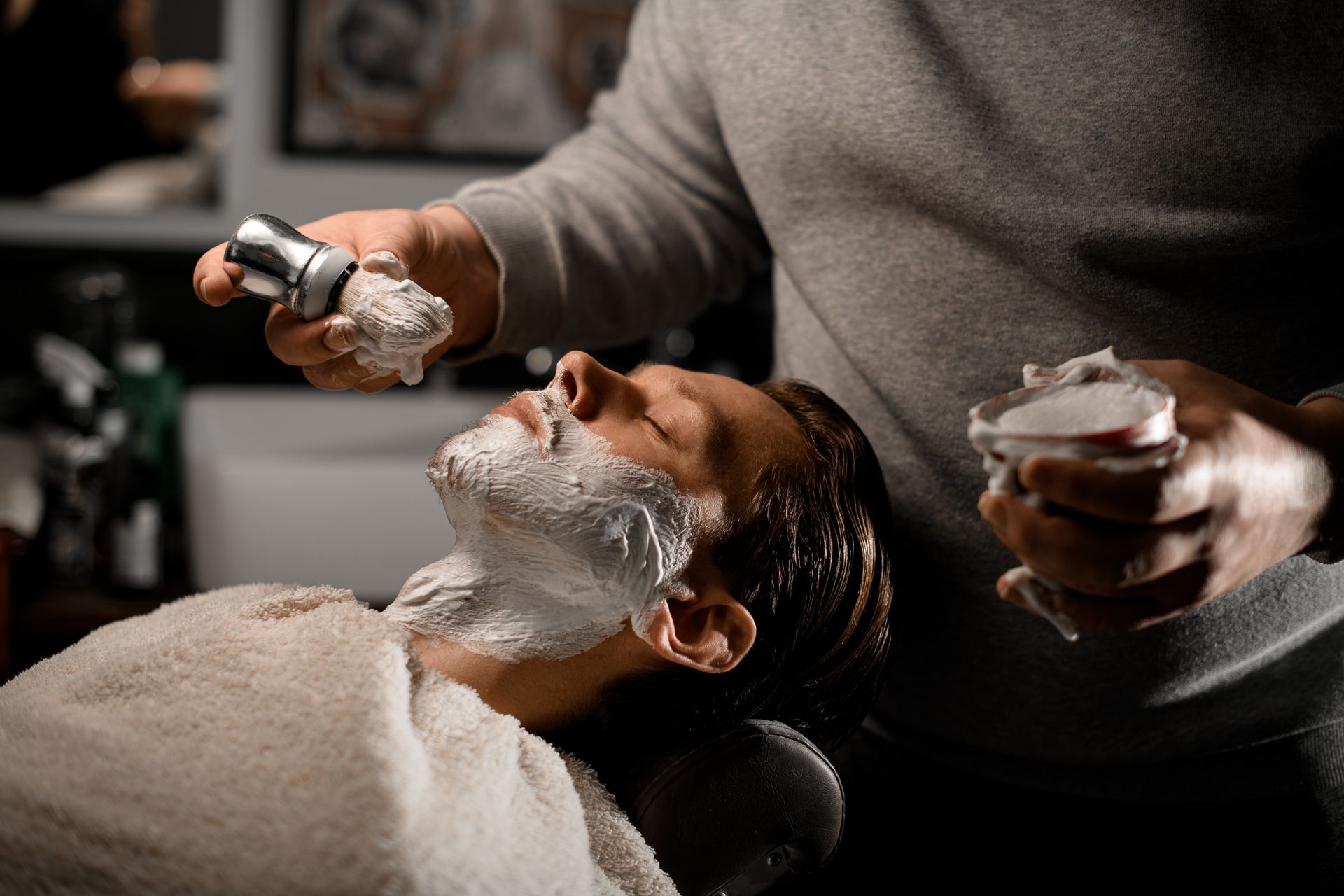 Barber shaving a customer's face with a straight razor and shaving cream in a salon