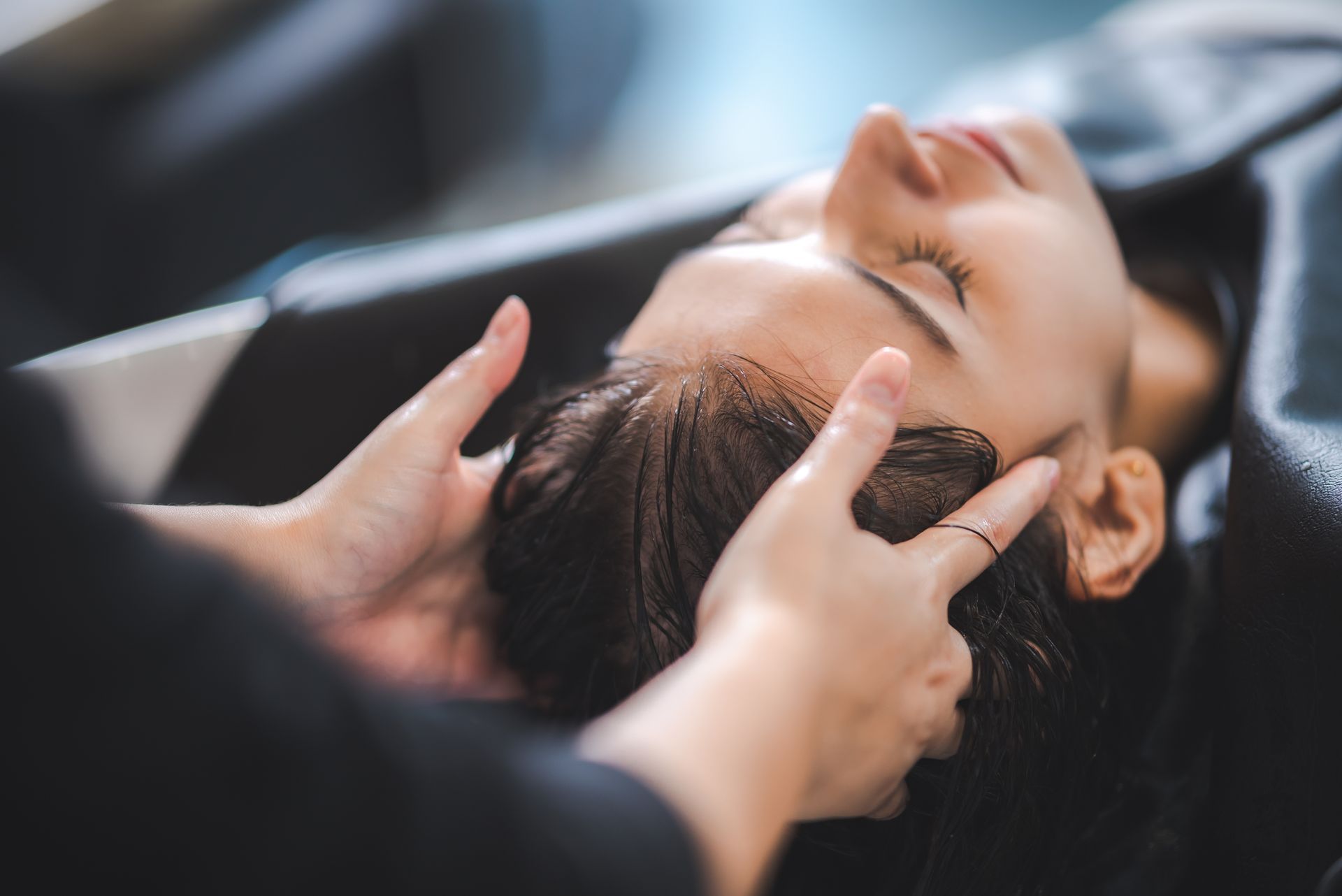 Hands gently support a reclining person’s head during a scalp massage.