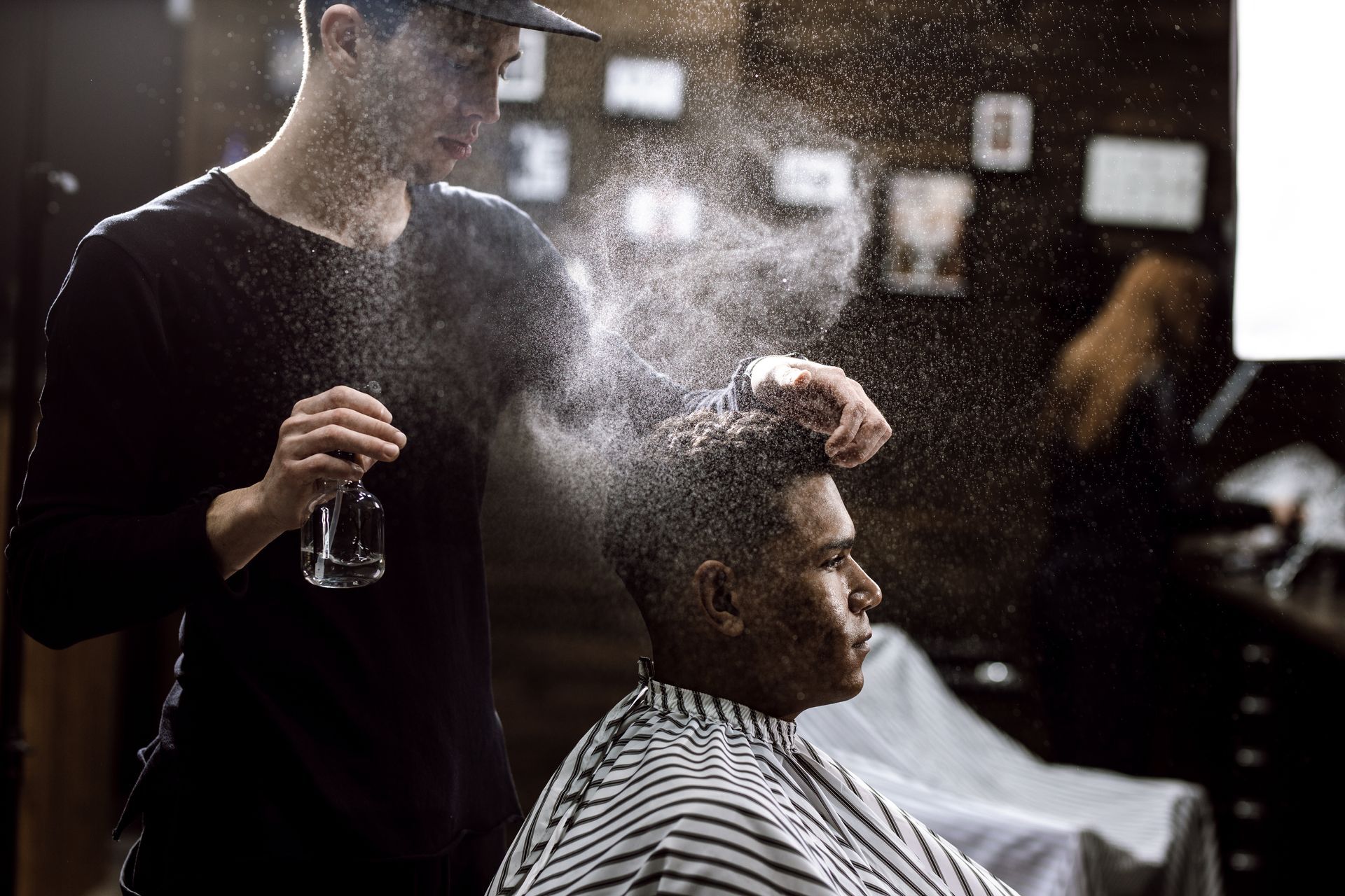 Hairdresser styling a seated client’s hair with spray in a barbershop