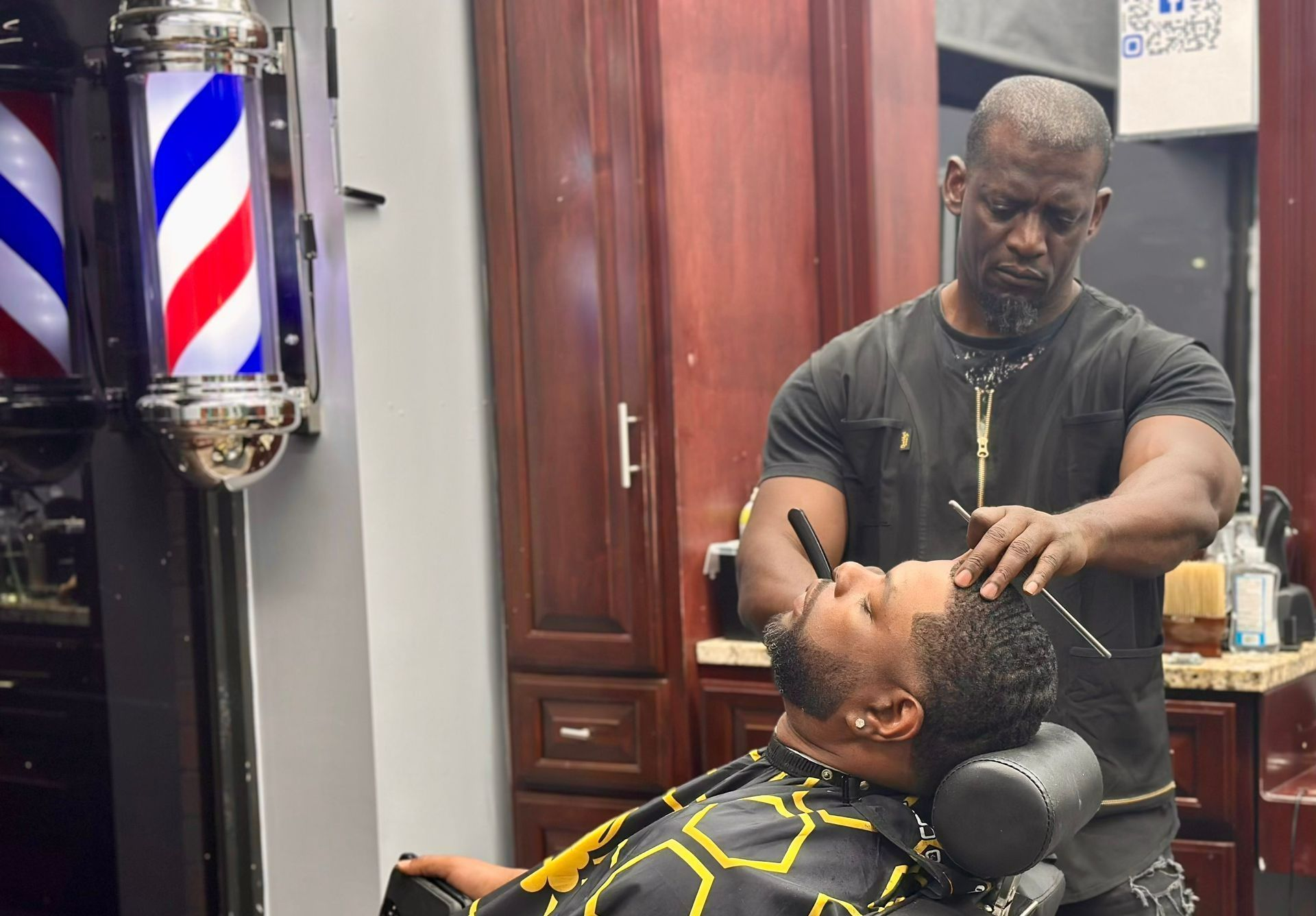 Barber trimming a client’s beard in a barbershop, with a red, white, and blue barber pole nearby