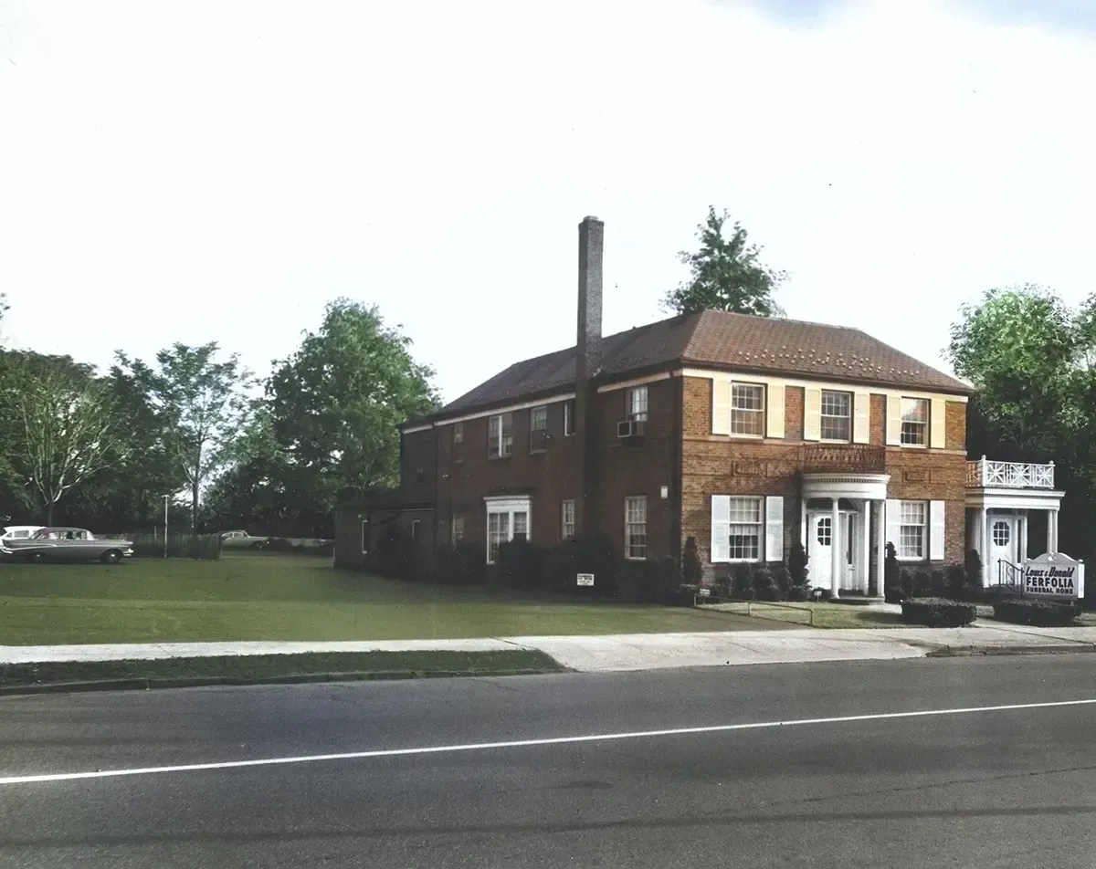 Two-story brick house with white trim beside a road, with a large lawn and trees in front.