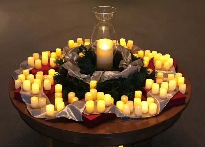 A candlelit wreath centerpiece with many small yellow candles around a large central candle on a round table