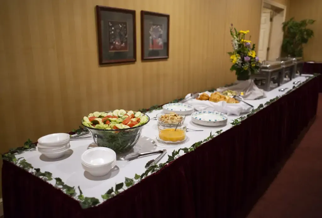 Buffet table with salads, fruit, and covered dishes along a wall in a banquet room