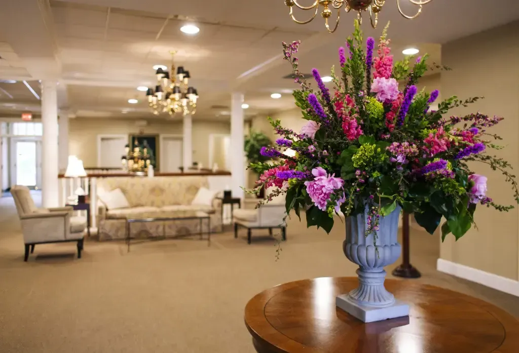 Elegant hotel lobby with chandeliers, beige seating, and a large pink-and-purple floral arrangement on a table