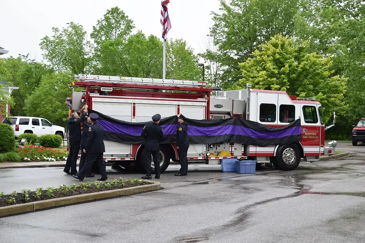 Firefighters carrying a folded purple inflatable rescue boat beside a red fire truck in a parking lot