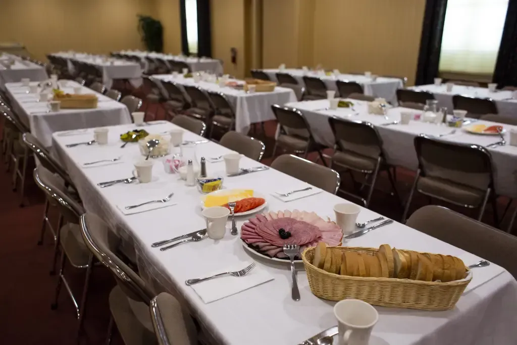 Banquet hall with long tables set for a meal, white tablecloths, and baskets of bread and pastries