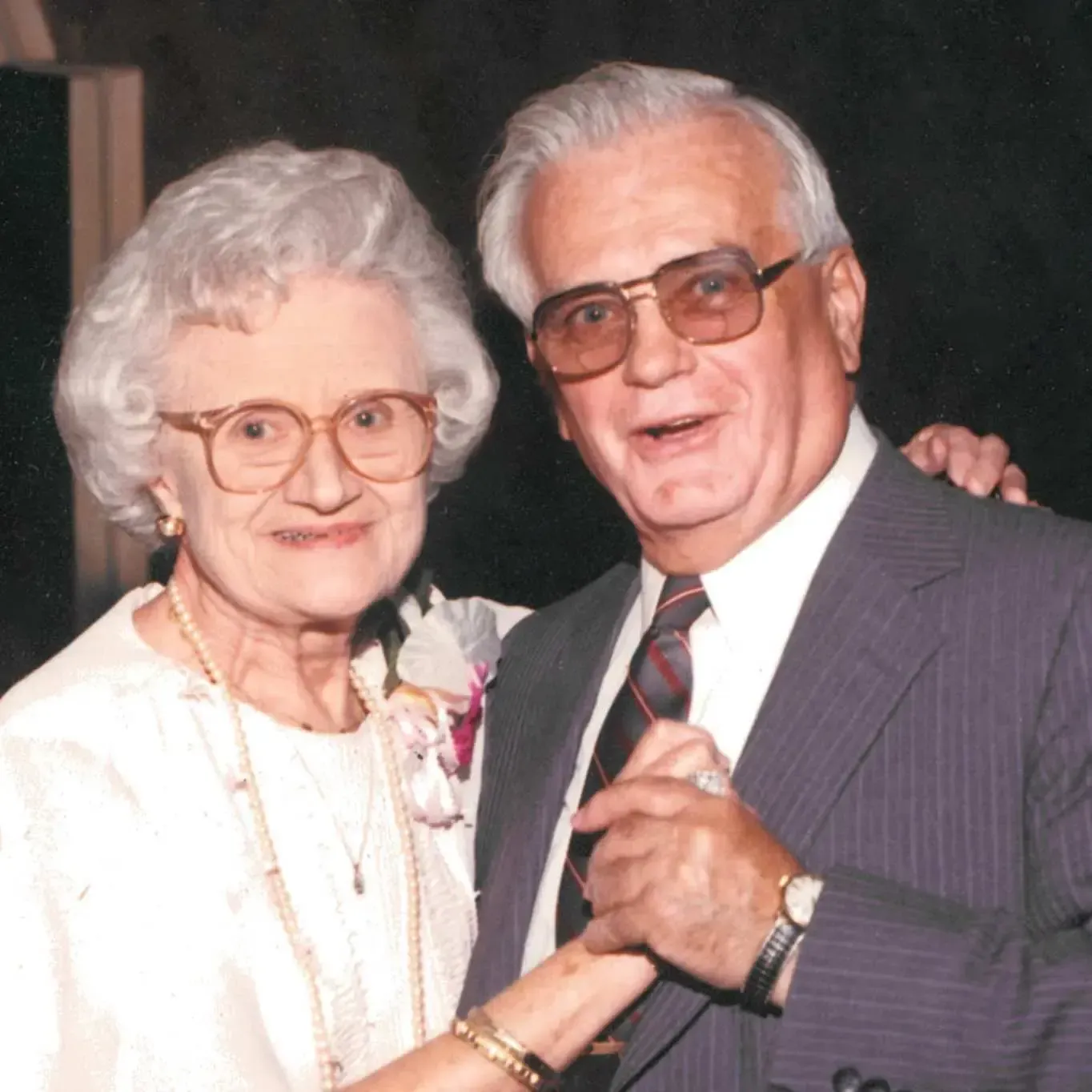 Elderly couple smiling and dancing, dressed formally at a social event.