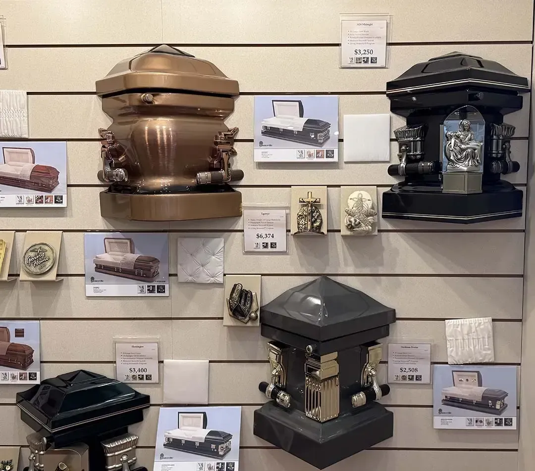 Display of ornate black and bronze memorial urns and keepsakes on a showroom wall with price cards