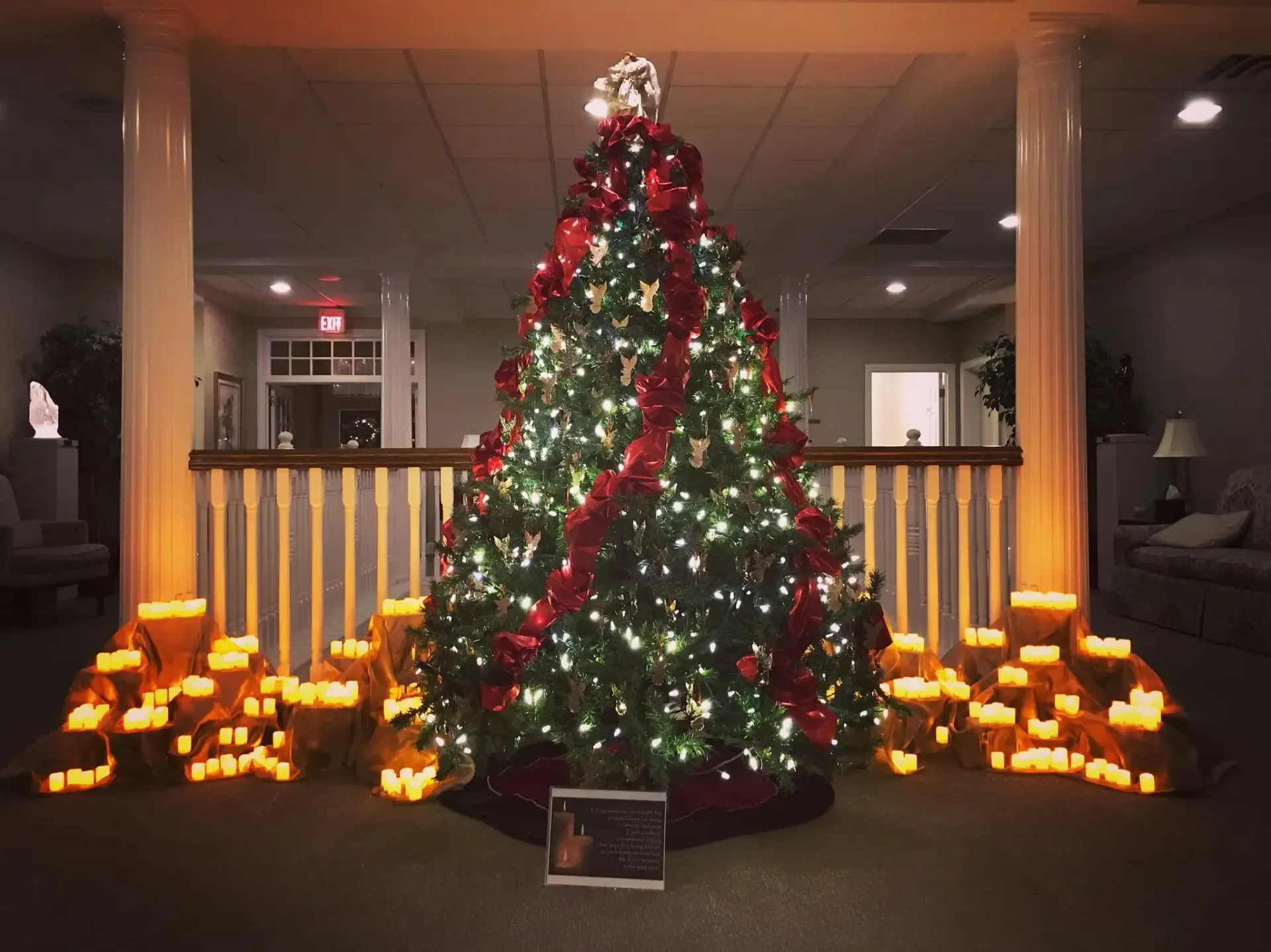 Decorated Christmas tree with red bows and lights, surrounded by glowing candles in a dim lobby