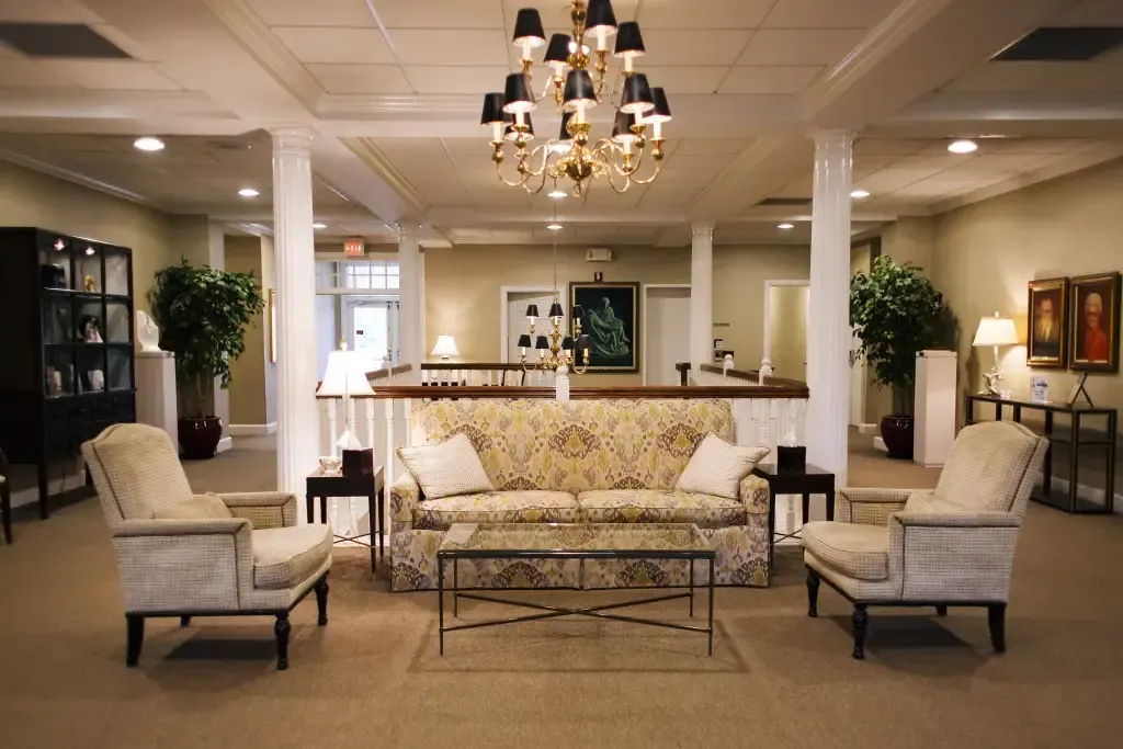Elegant hotel lobby with chandelier, white sofas, armchairs, and a bar in the background