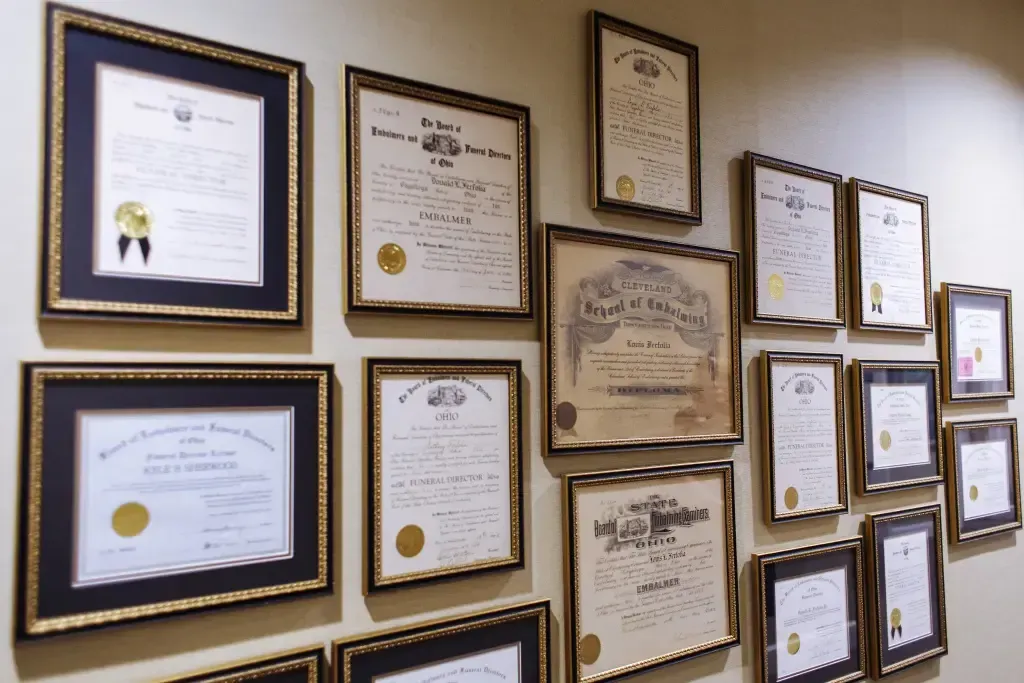Wall of framed certificates and awards on a beige wall, featuring blue, gold, and wood frames.