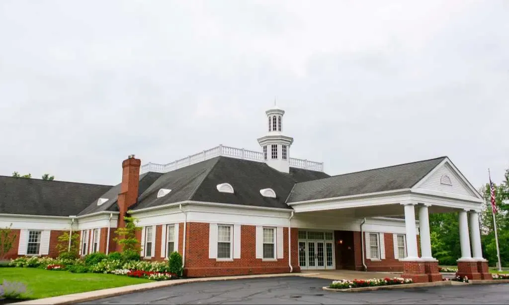 Brick building with white columns, red accents, and a cupola, seen from the front on a cloudy day