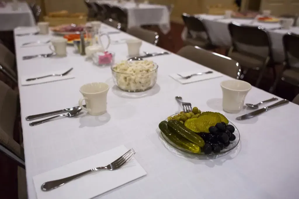 Banquet table set with plates, cups, and serving dishes of salad and pickles