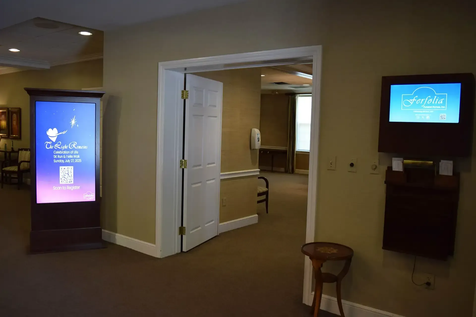Lobby with digital kiosks and wall-mounted screens near an open doorway.