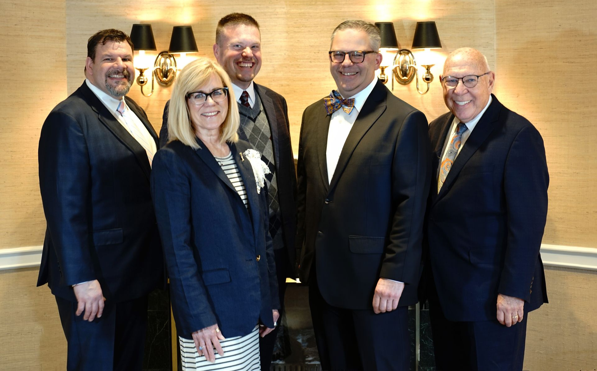Five people in business attire posing together indoors at a formal event.