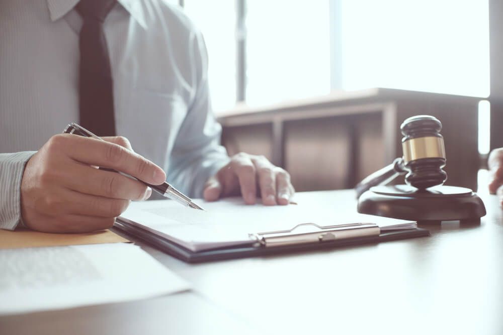 A Man Is Writing On A Clipboard Next To A Judge's Gavel — Farrell Lusher Solicitors In Wagga Wagga, NSW