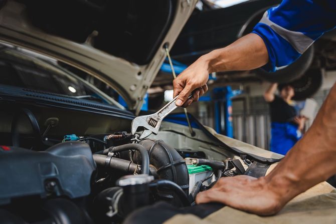 Mechanic using pliers to repair car engine under an open hood in a garage