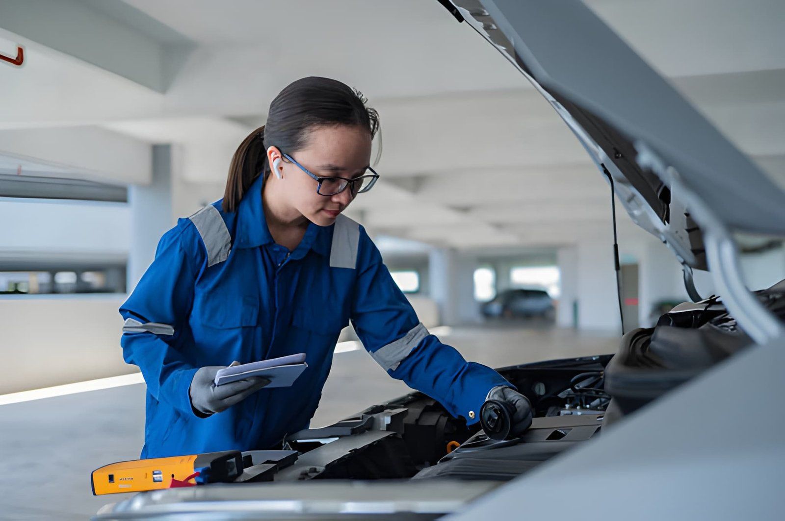 Mechanic in blue coveralls inspecting a car engine in a garage