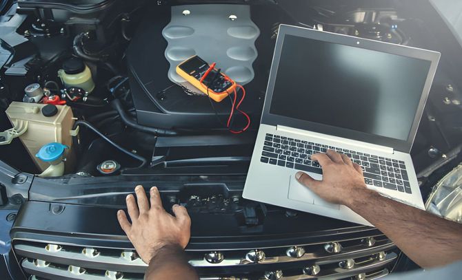 Mechanic using a laptop to diagnose a car engine in an open hood repair bay