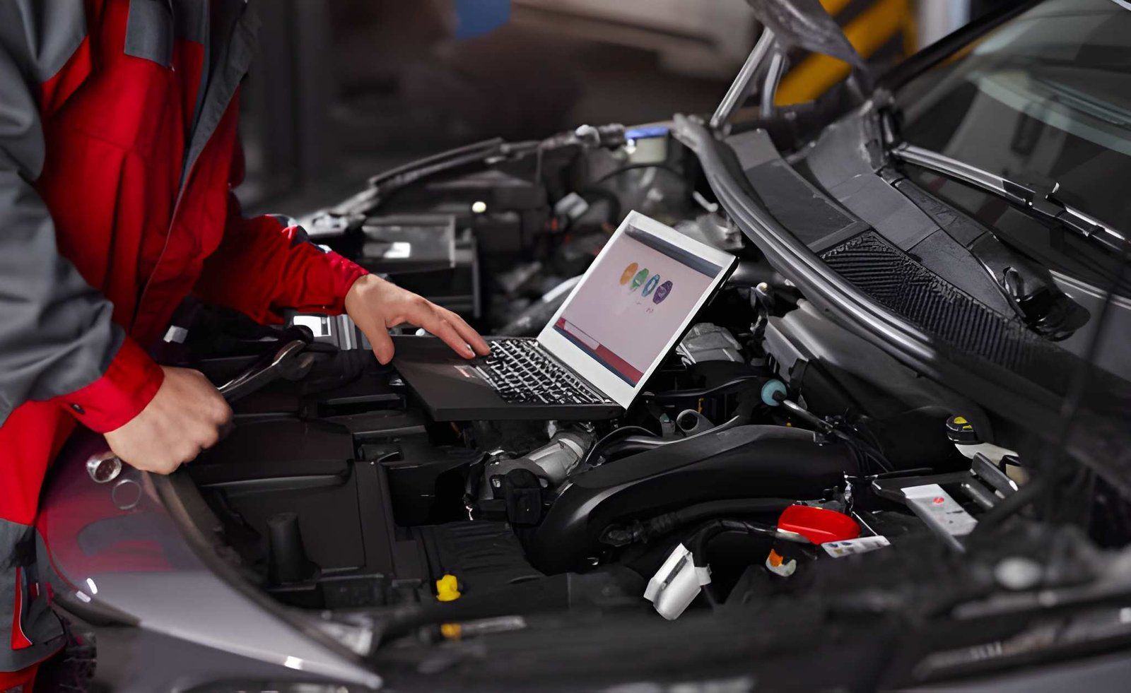 Mechanic using a laptop to diagnose a car engine in a garage