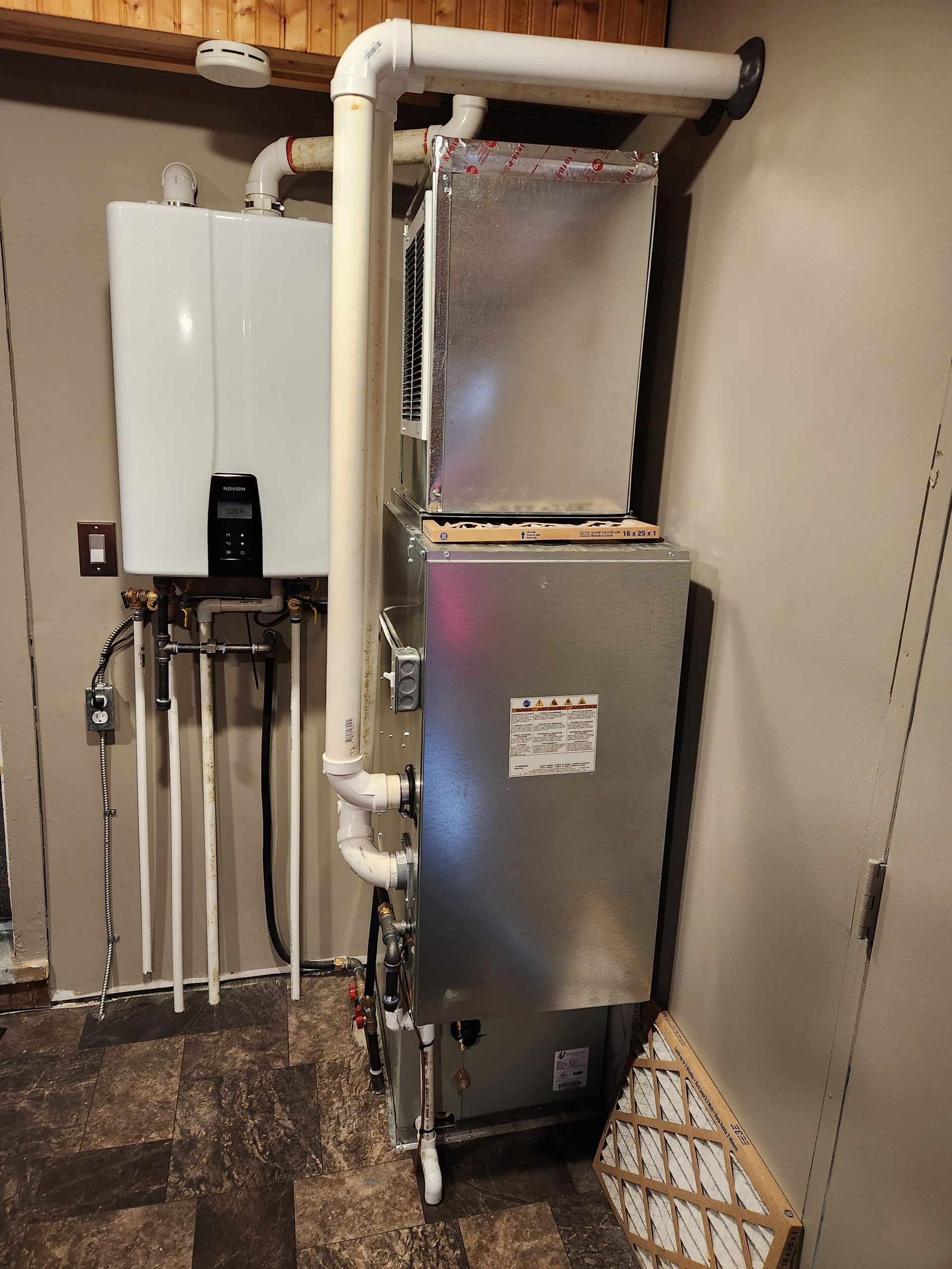 Furnace and water heater installation in a basement. White and silver equipment, neutral wall colors.