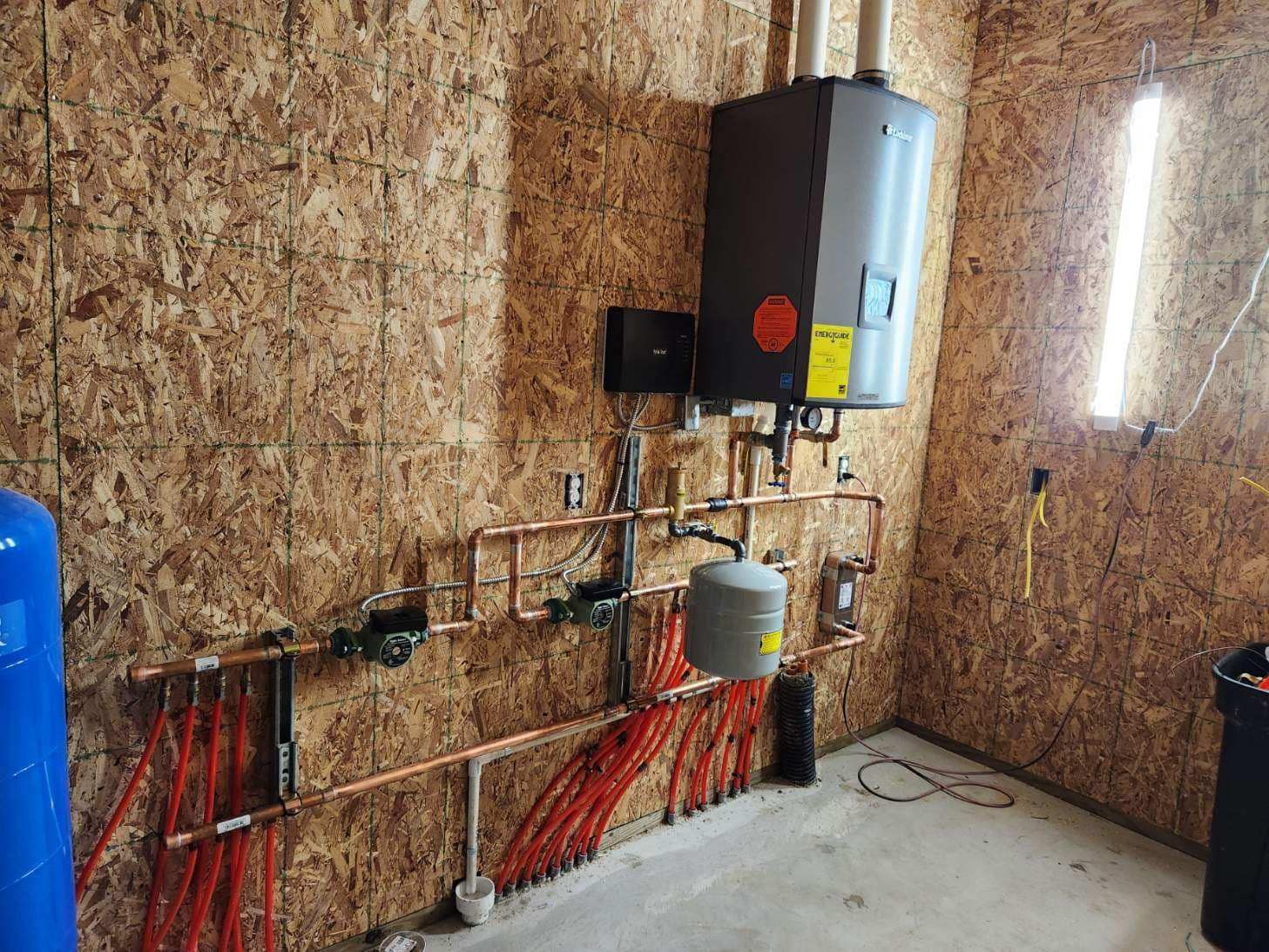 Copper pipes and a water heater installed on a wood wall in a utility room.