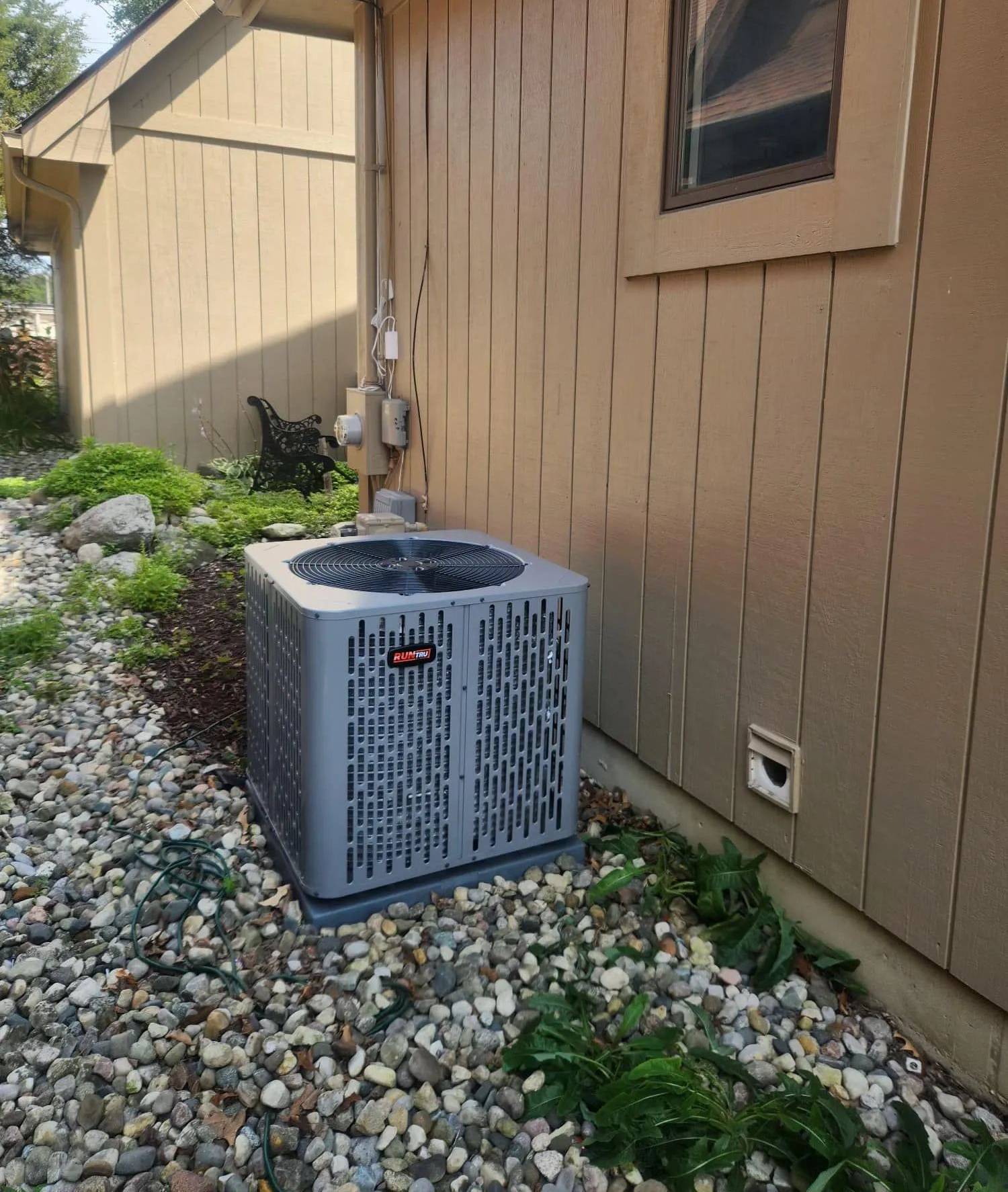 Outdoor air conditioner unit beside a tan house wall on a rocky landscaping bed