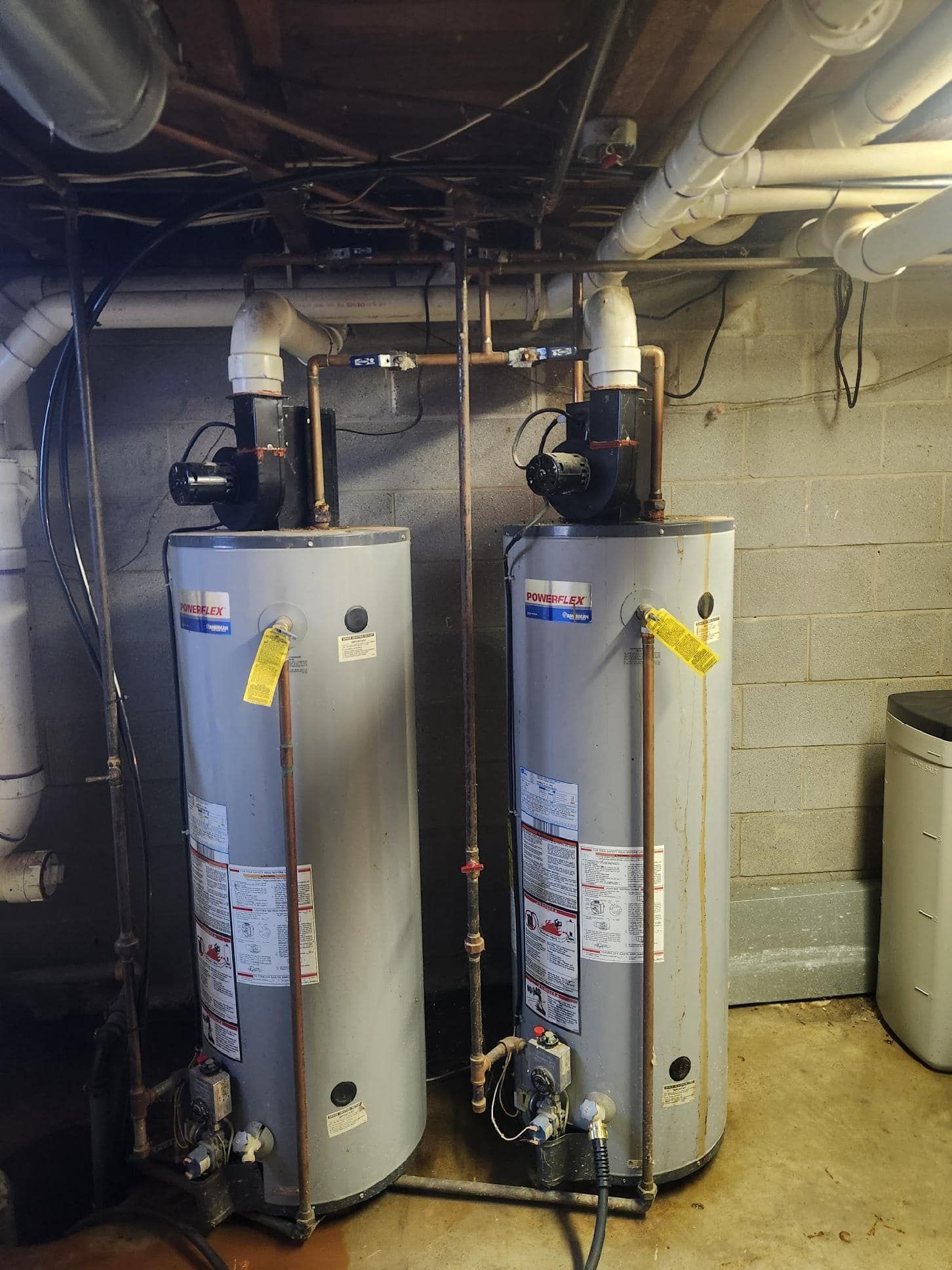 Two tall, gray water heaters with attached pumps and piping in a basement setting.