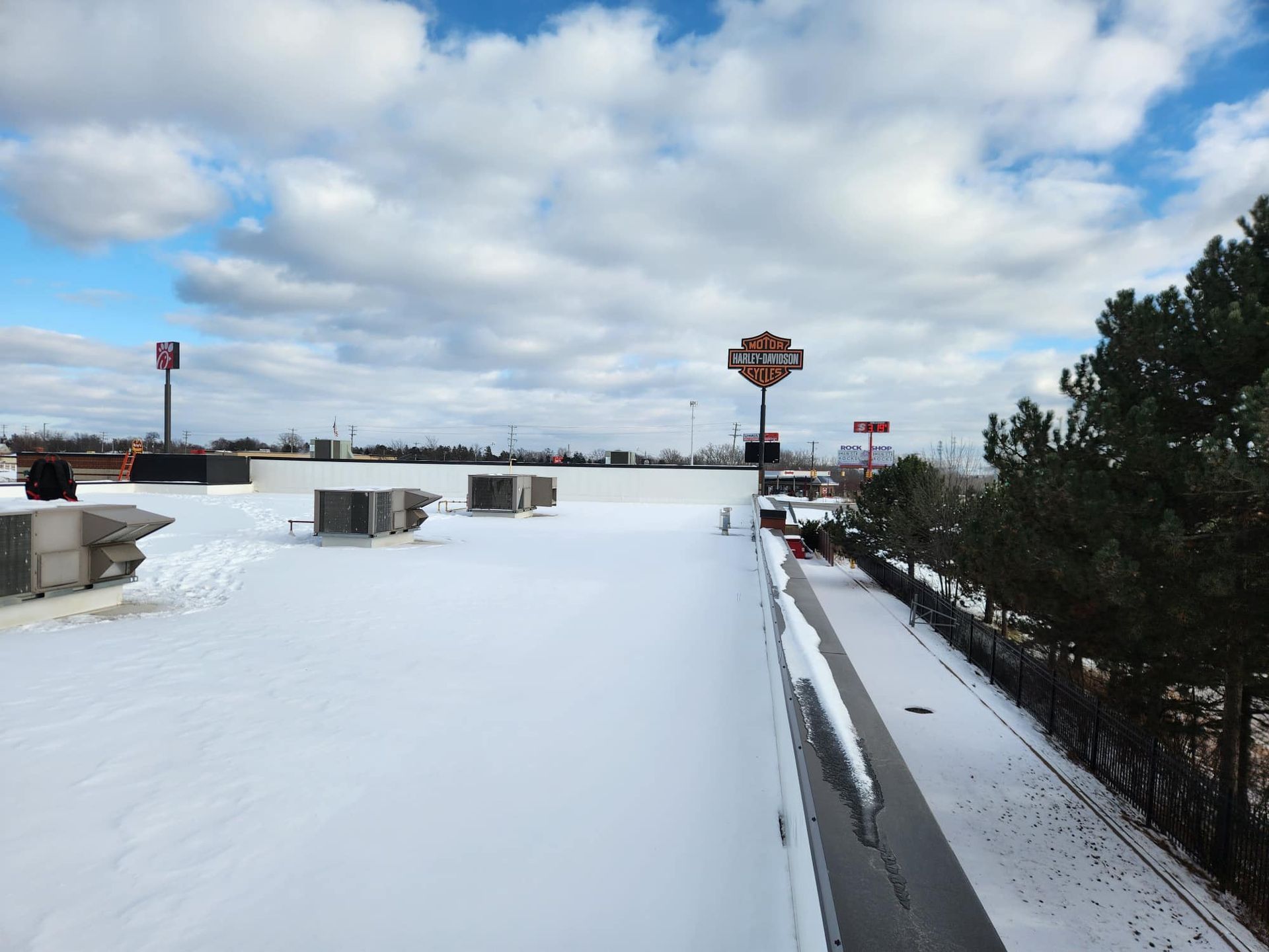 Snow-covered rooftop with a Harley Davidson sign visible under a cloudy sky.