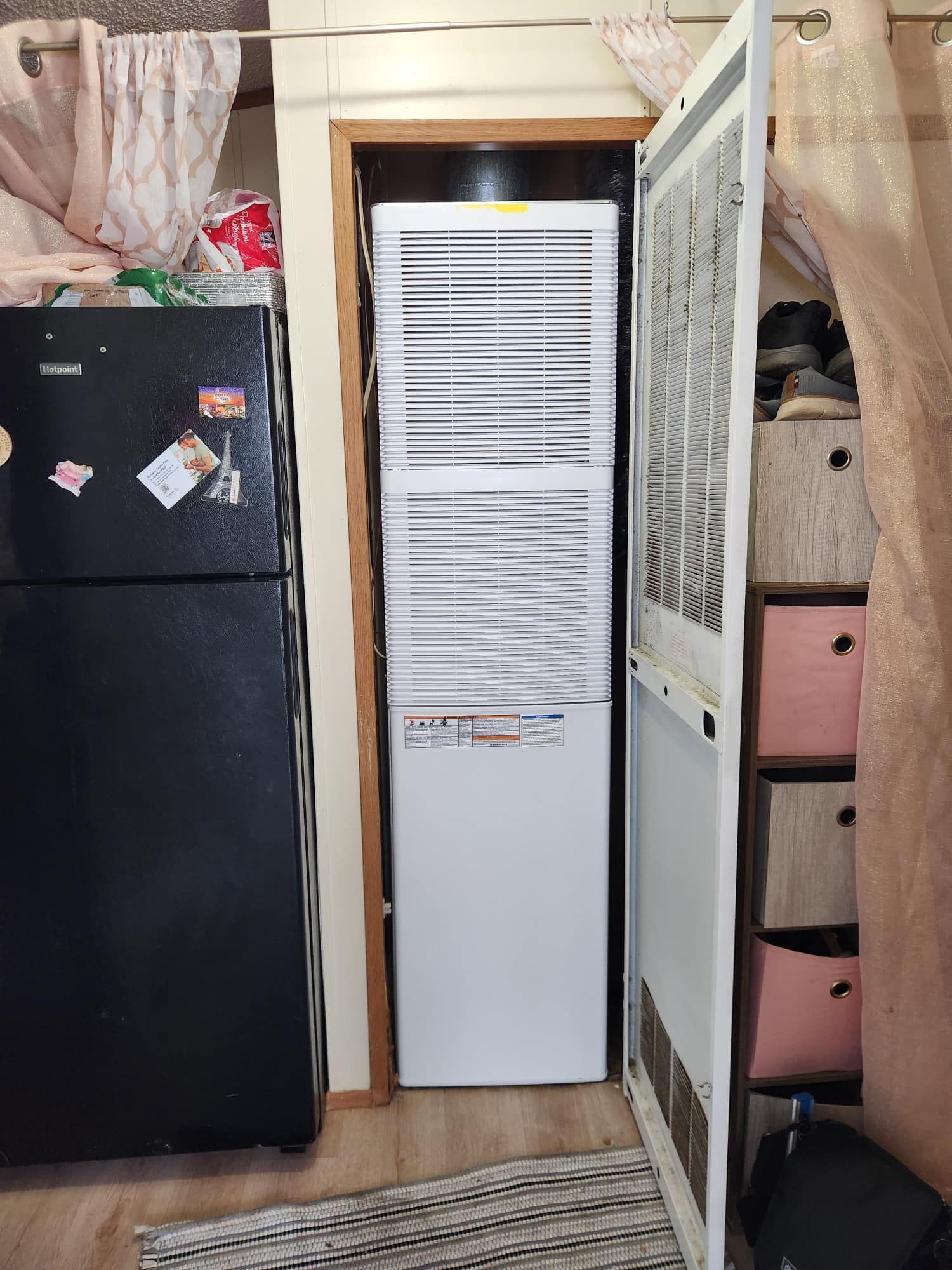 A black refrigerator and a tall furnace are next to each other. The furnace is white and the door is open.