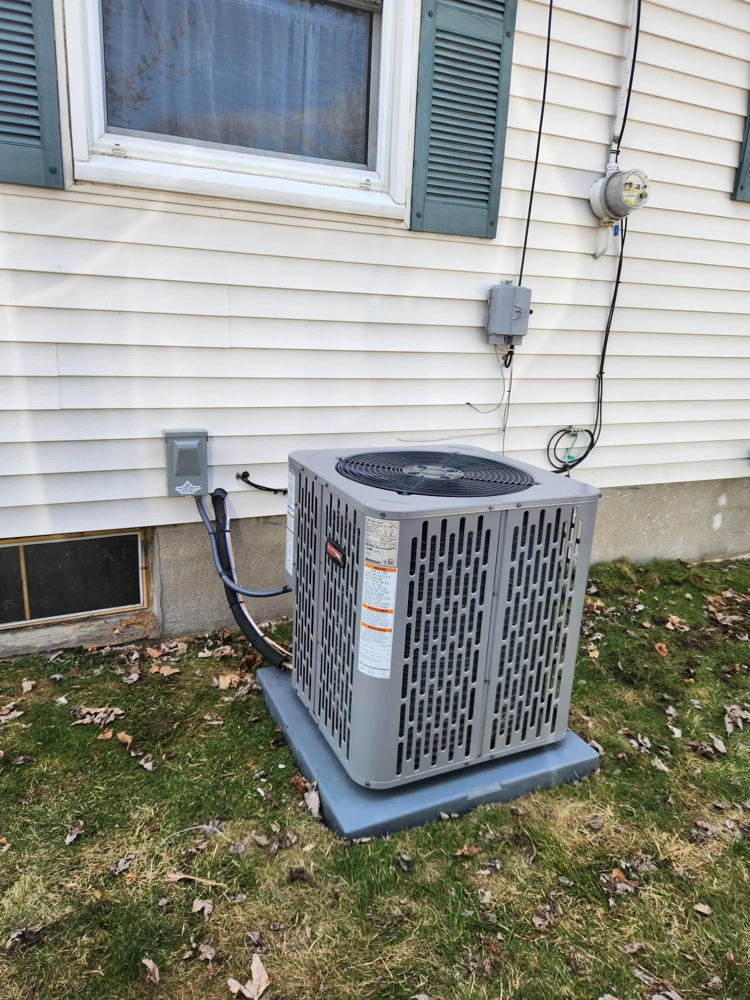 Outdoor air conditioner unit beside a house wall with white siding and a window above it