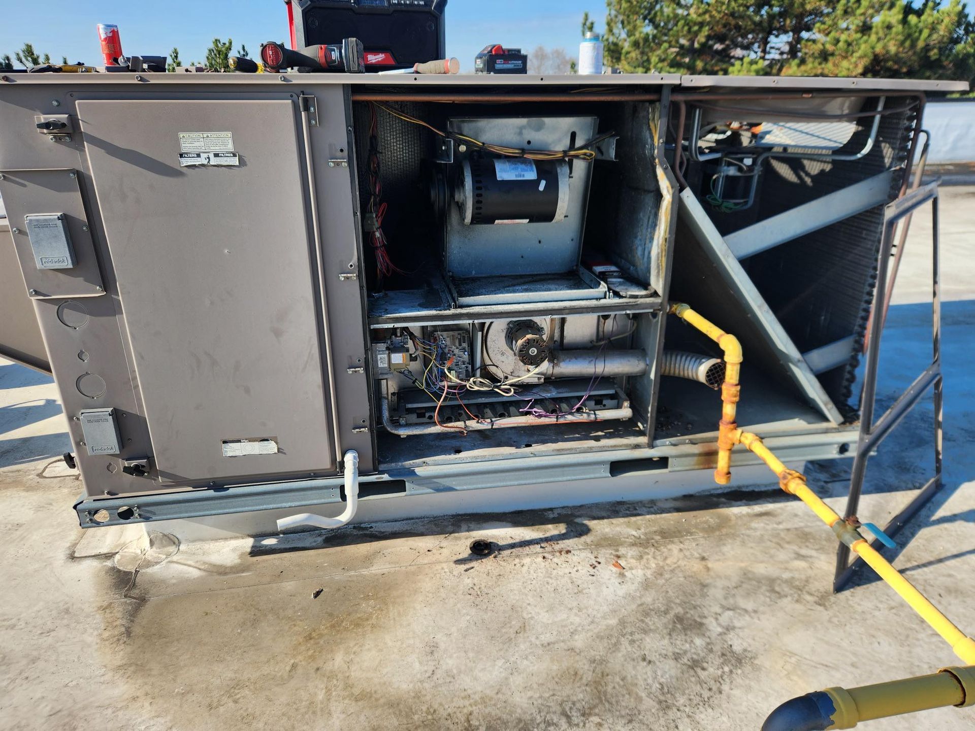 Open rooftop HVAC unit with exposed components. Yellow gas pipe and repair tools present.