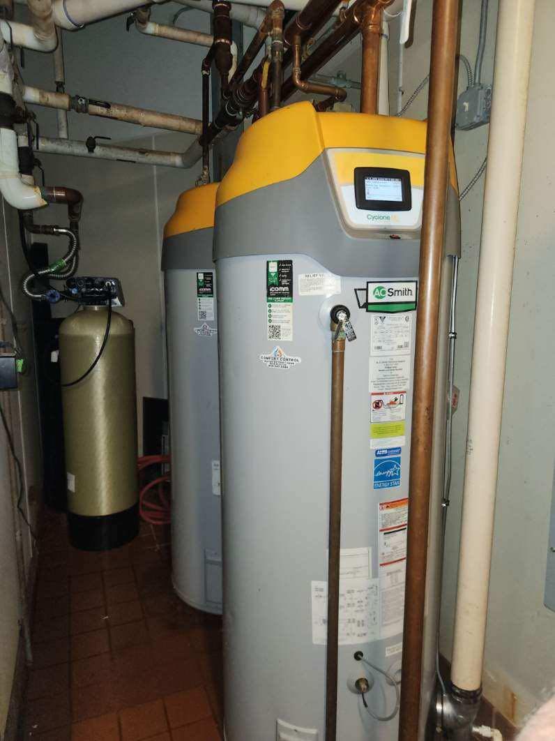 Two tall, cylindrical water heaters with yellow tops, next to a water softener in a utility room.