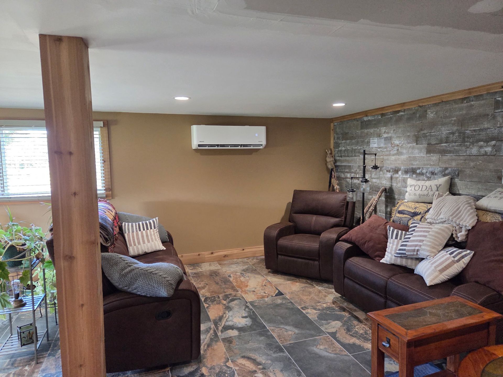 Cozy basement living room with brown reclining sofas, stone wall, and an air conditioner.