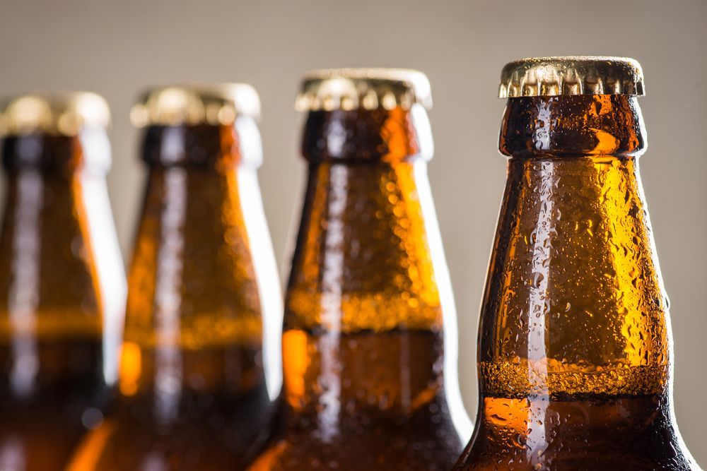Quattro bottiglie di birra ambrata in fila, con condensa.