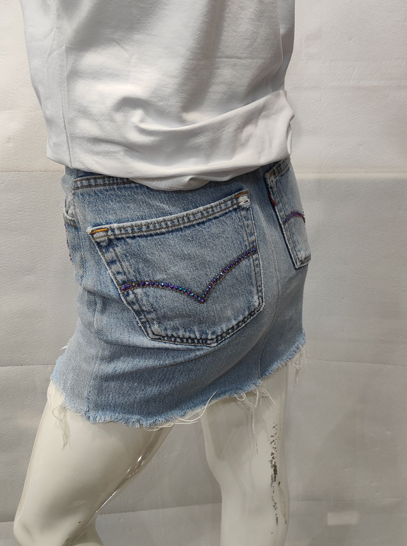 Gonna in denim chiaro con orlo sfrangiato e tasca posteriore con cucitura a V, indossata con top bianco su un manichino.
