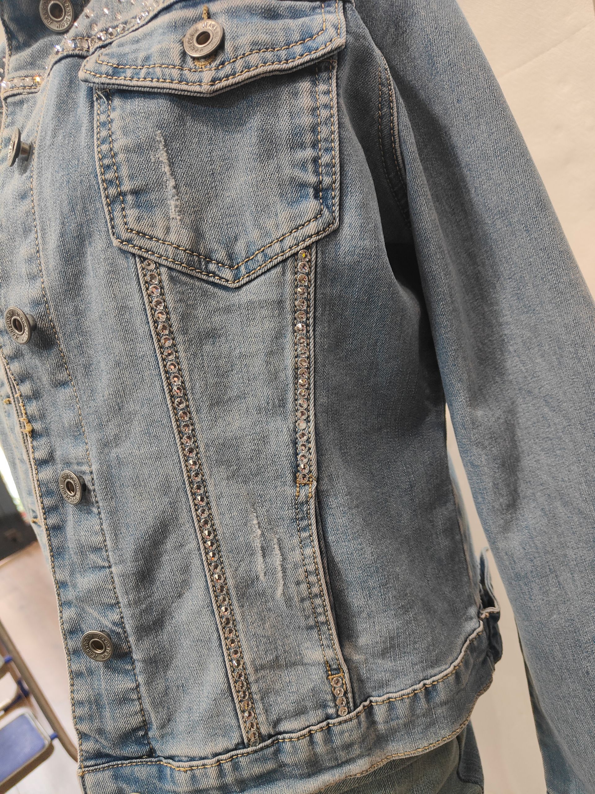 Primo piano di una giacca di jeans blu, tasche con bottoni e bottoni metallici lungo l'abbottonatura frontale.