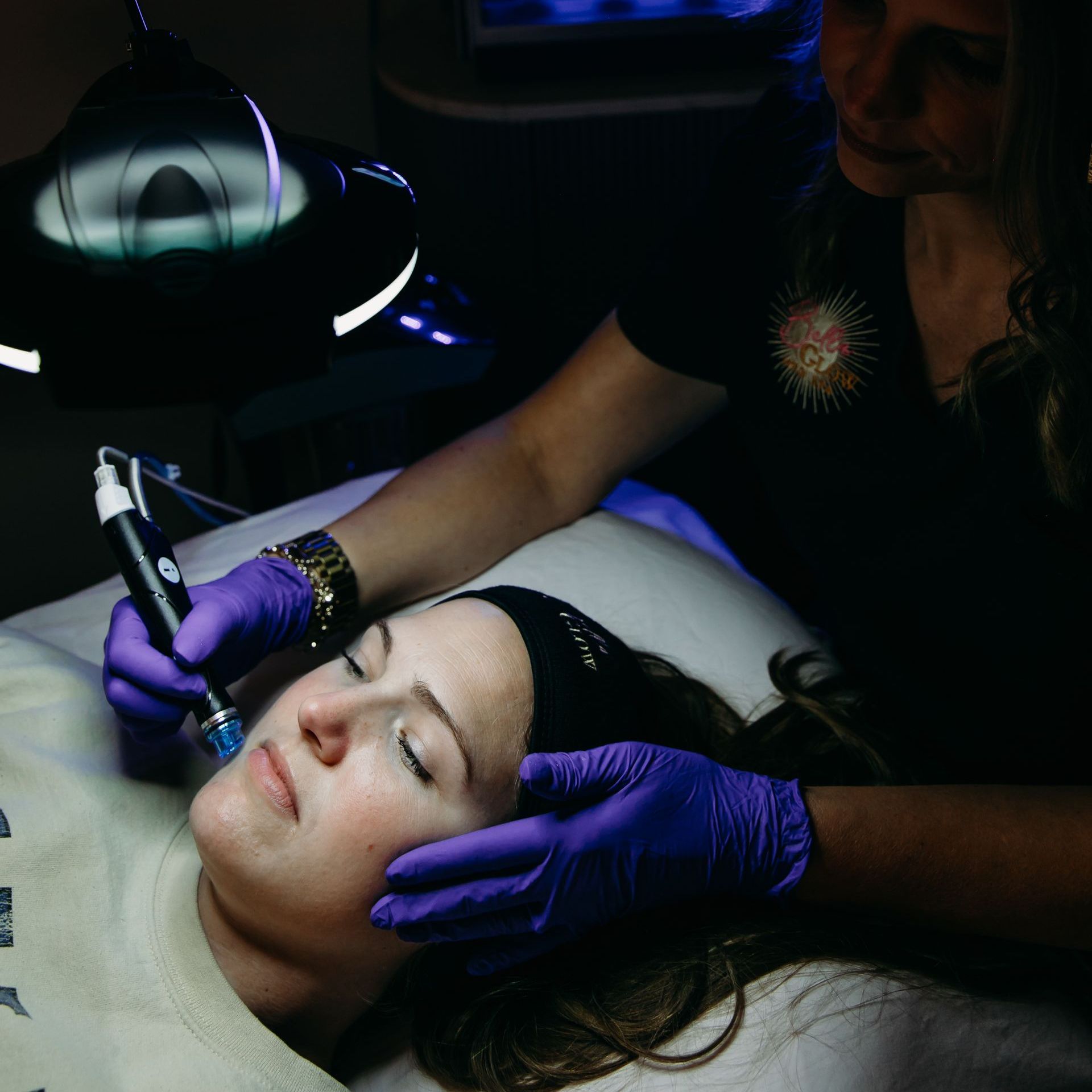 A woman in purple gloves is using a device on a woman 's face