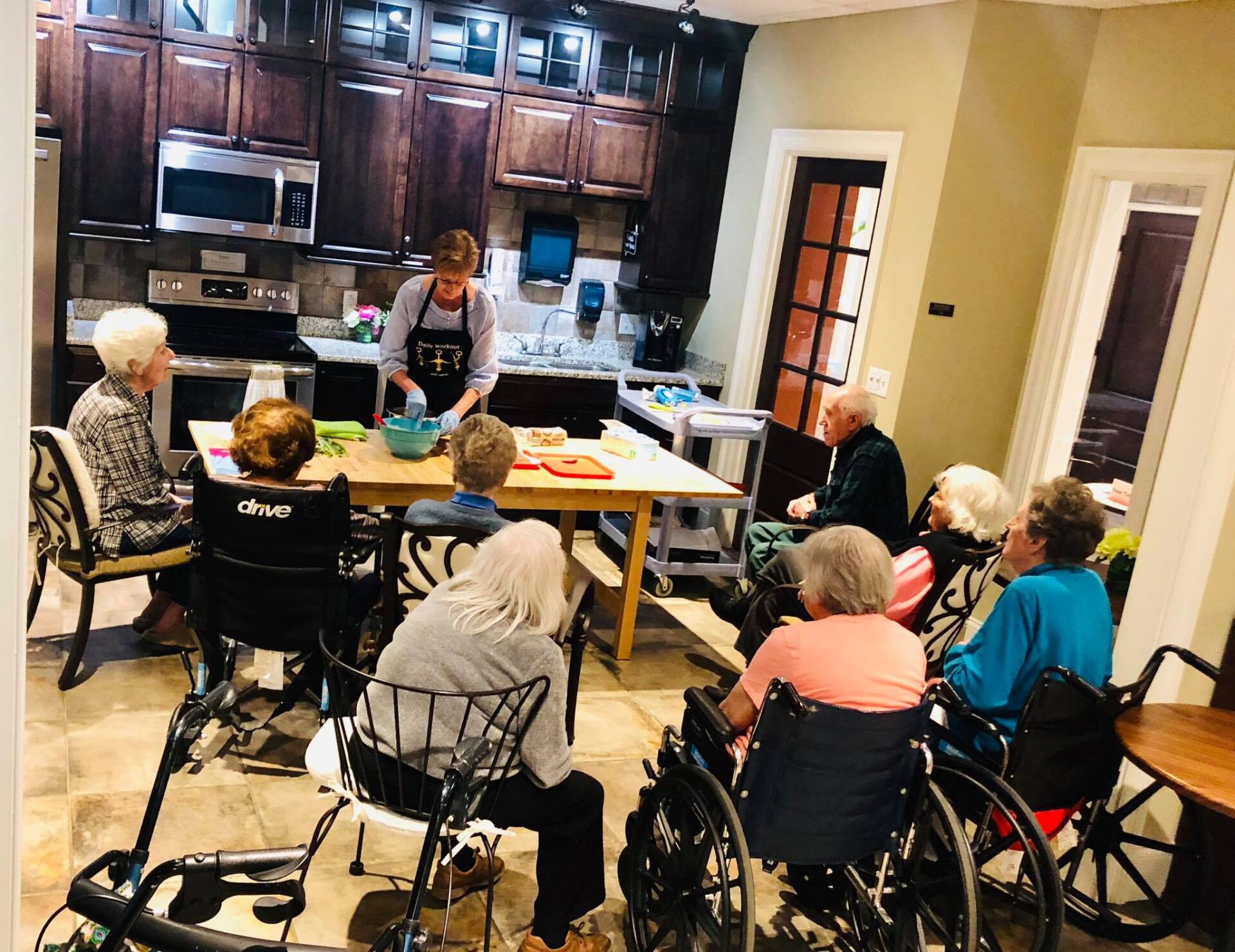 A facilitator leads a cooking activity for a group of people seated in a kitchen.