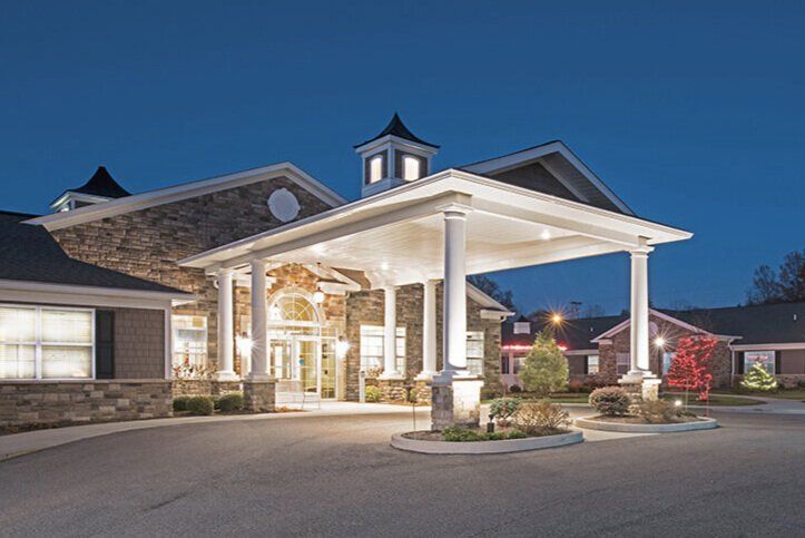 Stone building with a large covered entrance and columns at dusk, illuminated by exterior lighting.