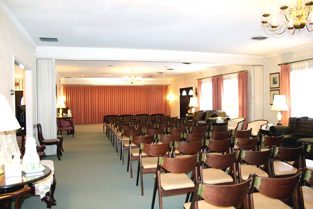 Rows of chairs face a curtained area in a formal room; a potential funeral service setting.
