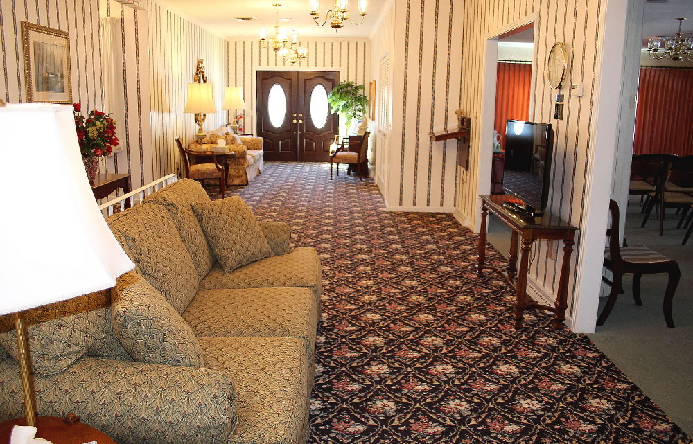 A waiting area with a sofa, floral carpet, striped wallpaper, and a TV.