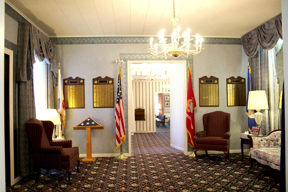 Hallway with flags, chairs, plaques, and a chandelier.