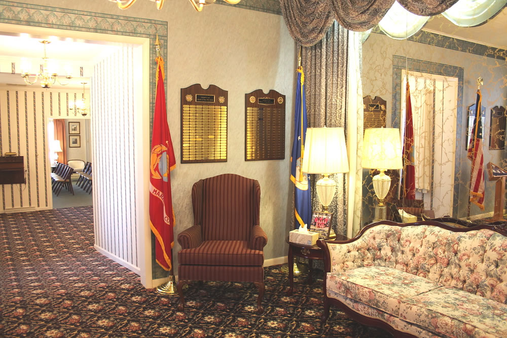 Interior with red Marine flag, wall plaques, floral sofa, wingback chair.