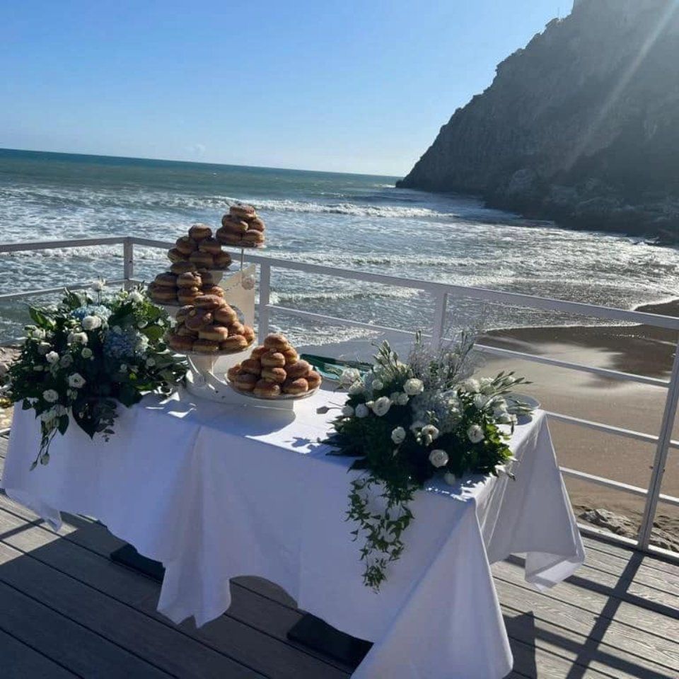 Tavolo con ciambelle e composizioni floreali su una terrazza con vista sull'oceano.